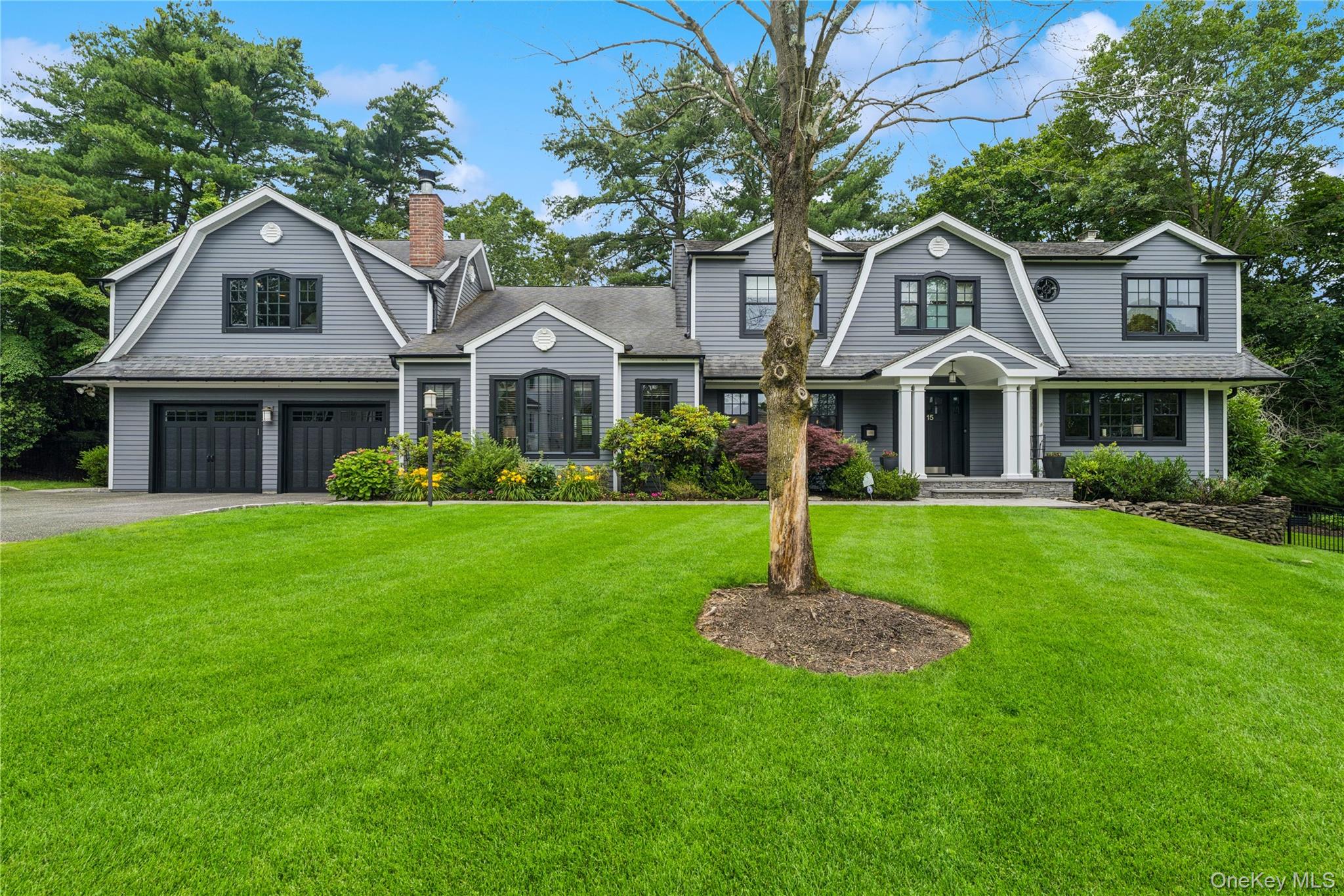 Shingle-style home with a gambrel roof, driveway, a front lawn, and a garage