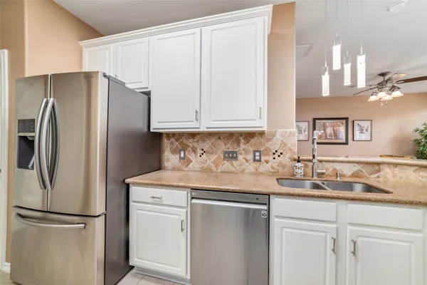 a kitchen with stainless steel appliances granite countertop a refrigerator a sink and white cabinets