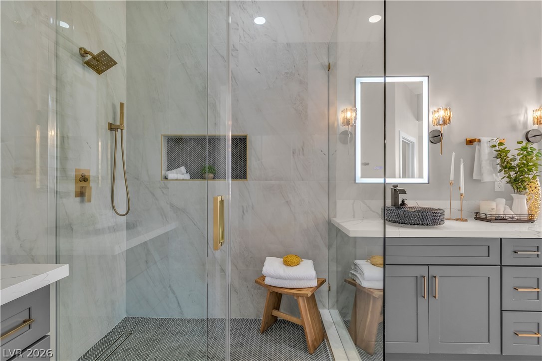 8848 Rainbow Ridge Drive Las Vegas, NV 89117 - Photo 35 of 43 Elegant shower and vanity featuring gold-toned fixtures and herringbone-patterned tile flooring.