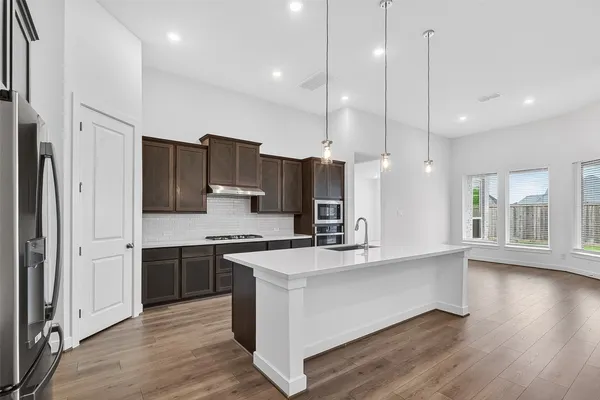 a large kitchen with stainless steel appliances kitchen island granite countertop a stove a refrigerator a sink and a wooden floor