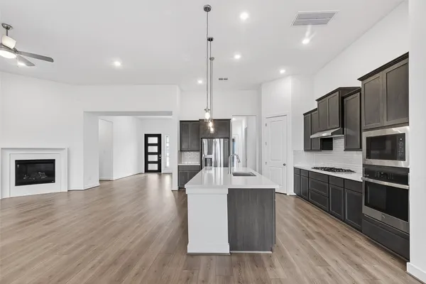 a kitchen with stainless steel appliances kitchen island granite countertop a stove top oven a sink dishwasher a refrigerator and a fireplace with wooden floor