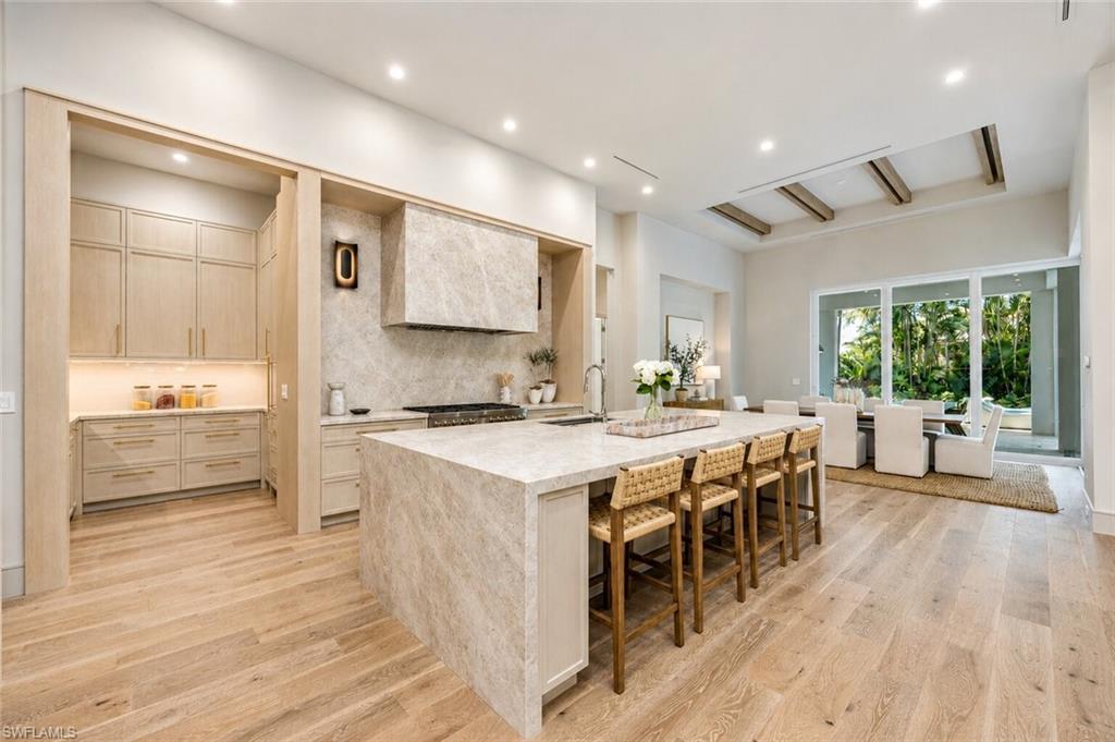 4851 Crayton Road Naples, FL 34103 - Photo 10 of 33 Open-concept kitchen featuring an expansive island with waterfall edge, wood-finish flooring, integrated range hood, recessed lighting, and a separate pantry area