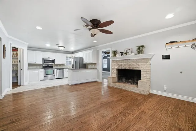 a view of a livingroom with a fireplace a ceiling fan and wooden floor