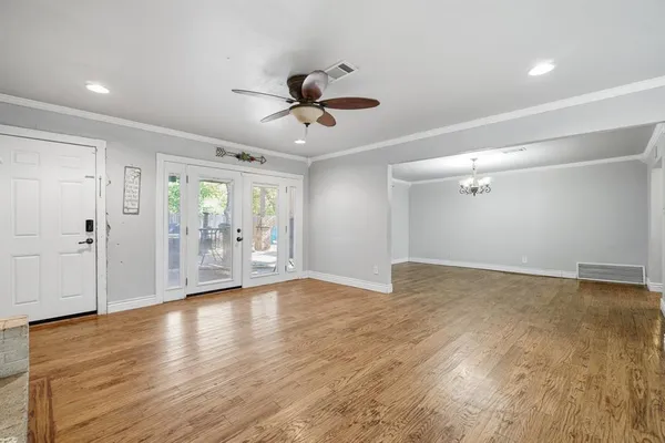 a view of an empty room with wooden floor and a ceiling fan
