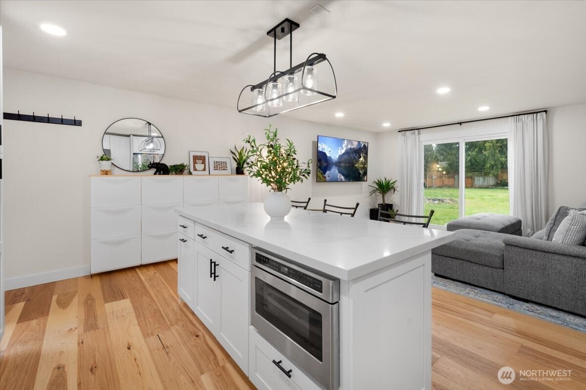 6131 86th Street Northeast Marysville, WA 98270 - Photo 8 of 22 a kitchen with stainless steel appliances a sink dishwasher a microwave oven a dining table and chairs with wooden floor