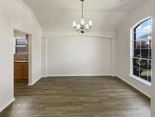 a view of an empty room with wooden floor and kitchen view