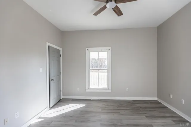 a view of an empty room with window and hardwood floor