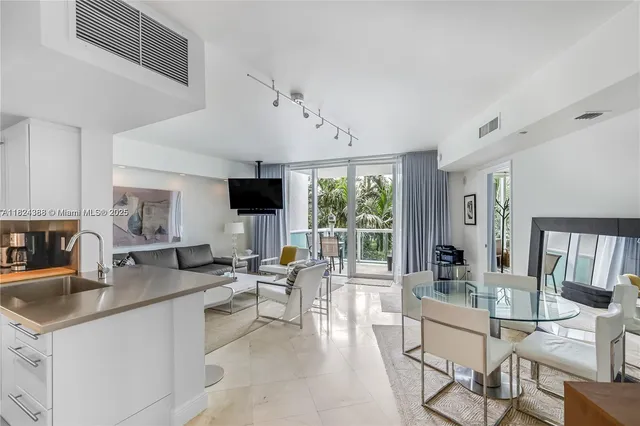 a dining hall with stainless steel appliances kitchen island granite countertop a table chairs in it and a flat screen tv