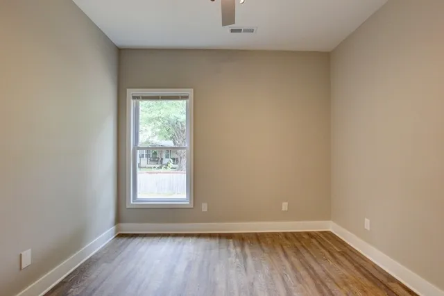 an empty room with wooden floor chandelier fan and windows