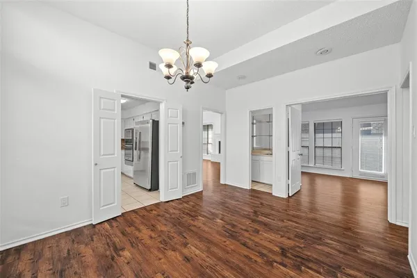 a view of an empty room with wooden floor and kitchen view