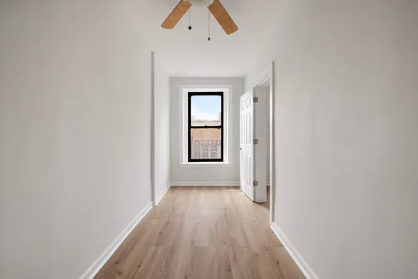 an empty room with wooden floor chandelier fan and windows