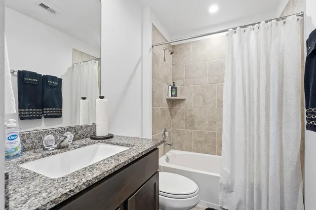 a bathroom with a granite countertop bathtub shower sink vanity and toilet