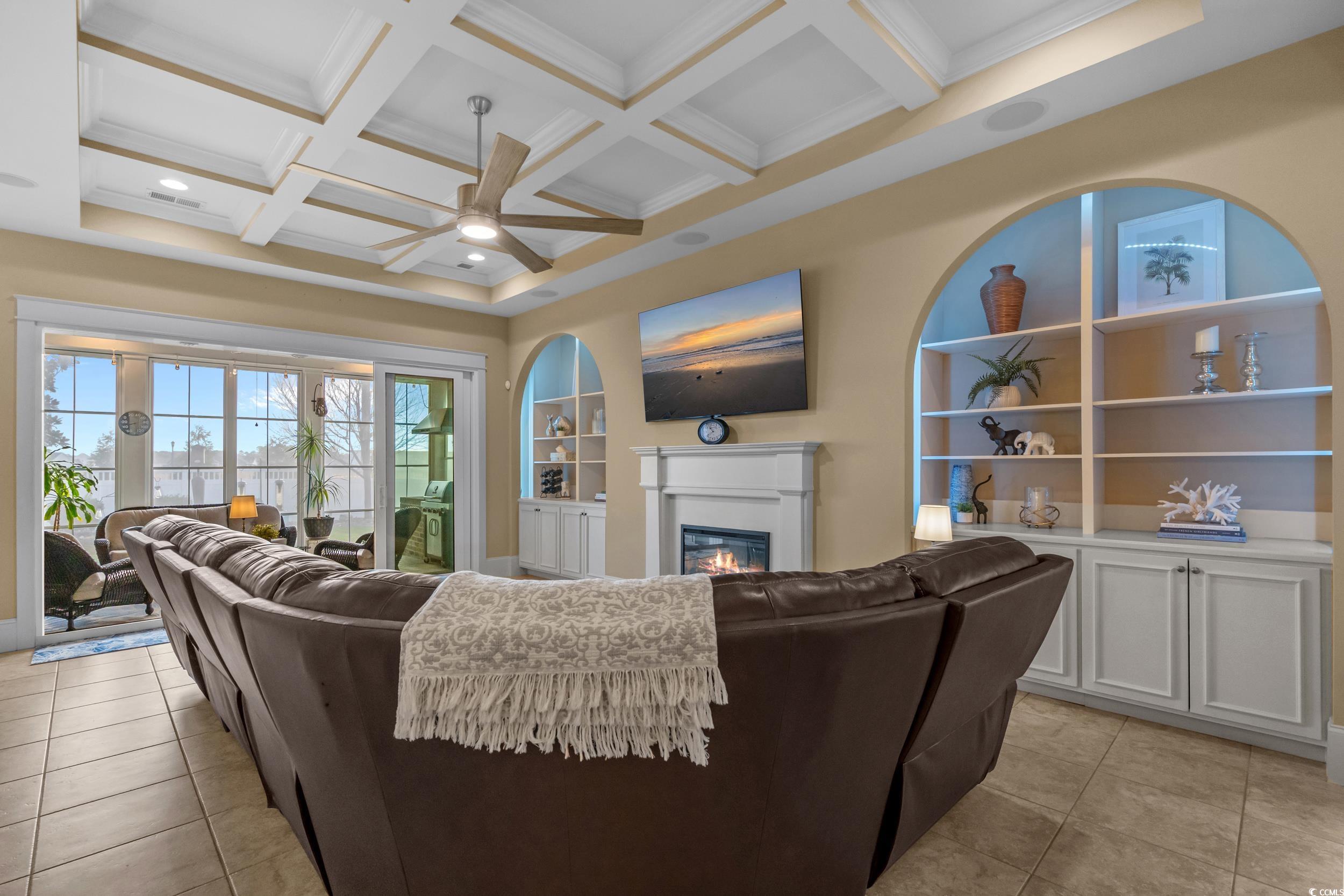 2604 Painted Trillium Court Myrtle Beach, SC 29579 - Photo 13 of 40 Living room featuring a glass covered fireplace, built in features, light tile patterned floors, coffered ceiling, and ceiling fan