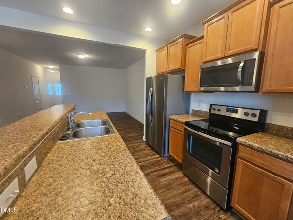 a kitchen with stainless steel appliances granite countertop a refrigerator a stove and a sink with wooden floor