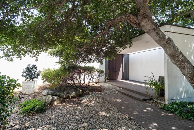 a pathway of a house with potted plants and large trees