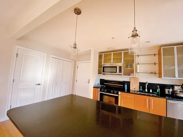 a kitchen with stainless steel appliances granite countertop a stove a sink a refrigerator a dining table and white cabinets with wooden floor