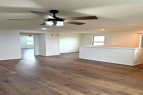 a view of an empty room with wooden floor and a ceiling fan