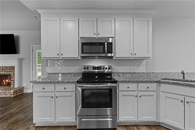 a kitchen with granite countertop white cabinets and a stove a oven with wooden floor
