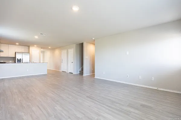 a view of an empty room with wooden floor and kitchen