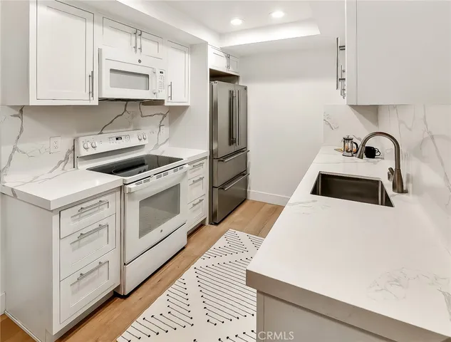 a kitchen with stainless steel appliances a stove a sink a refrigerator white cabinets and wooden cabinets