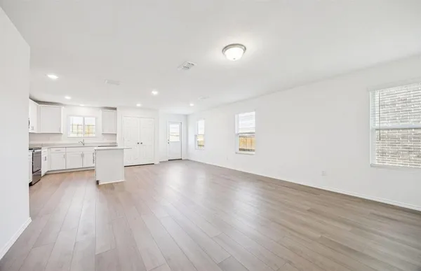 a view of an empty room and a kitchen with wooden floor and windows