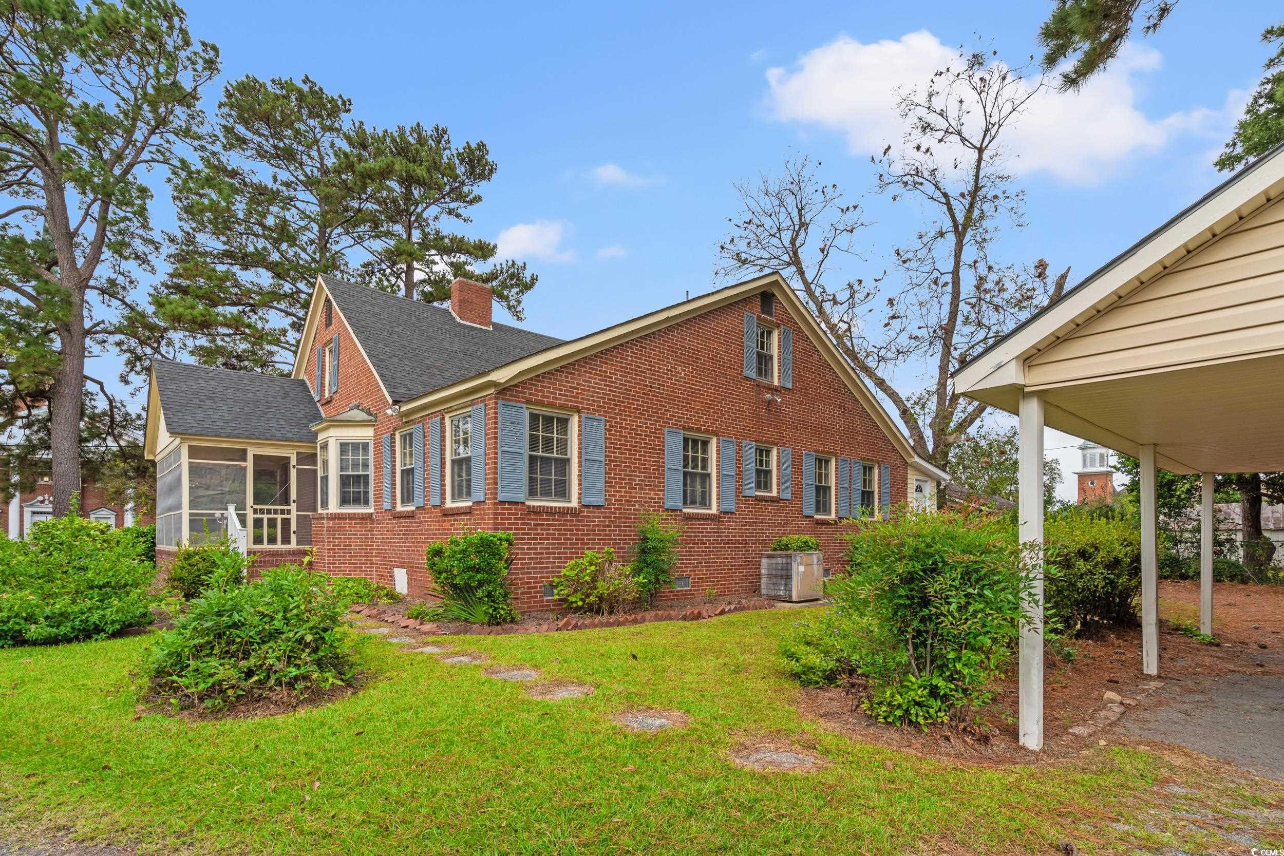 310 North Main Street Mullins, SC 29574 - Photo 9 of 35 View of property exterior featuring a chimney, a sunroom, a lawn, brick siding, and a shingled roof