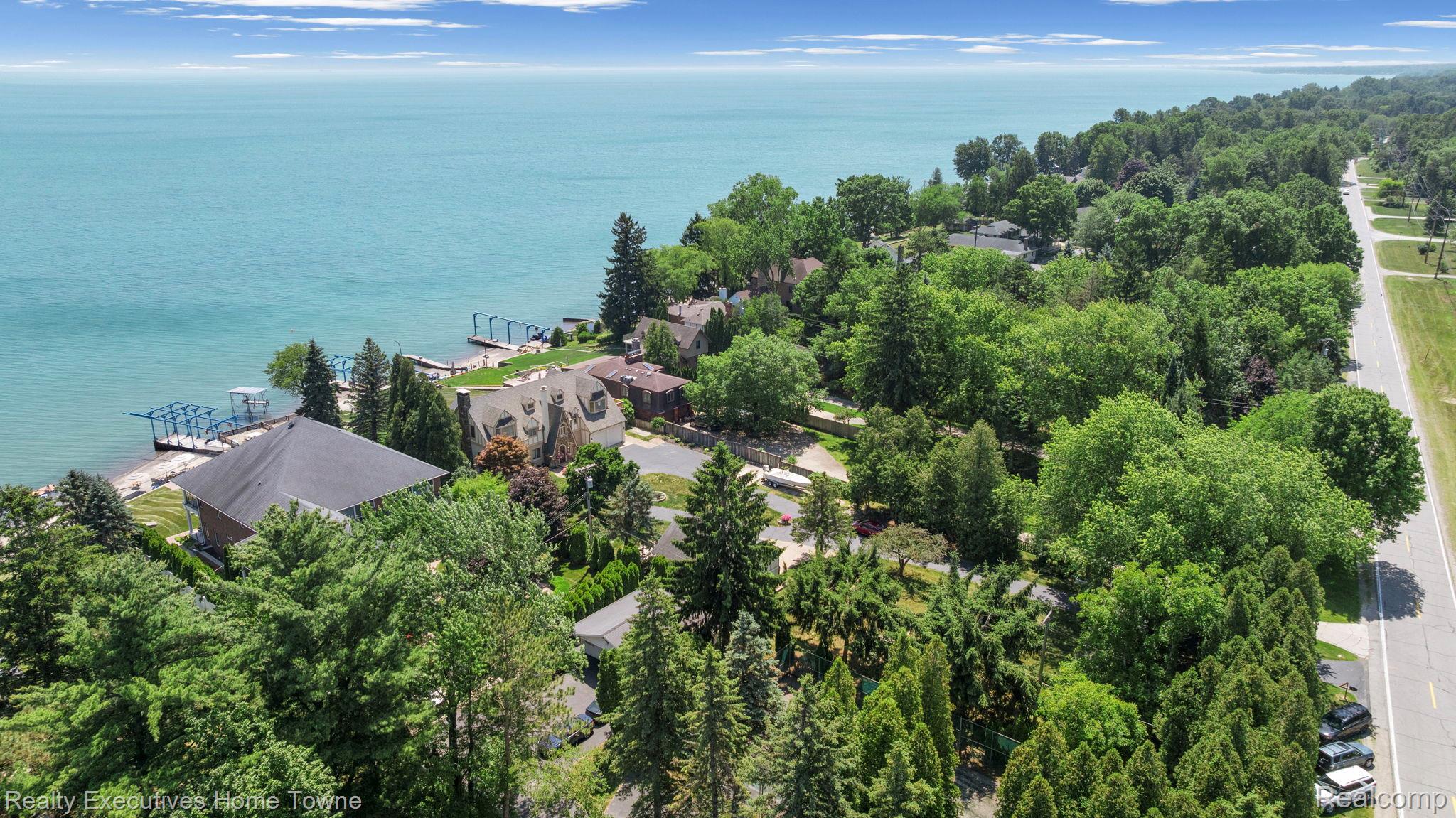 8308 Lakeshore Road Fort Gratiot, MI 48059 - Photo 23 of 79 Aerial perspective showcasing shoreline properties with private docks, a paved road bordering the tree line, and extensive mature landscaping