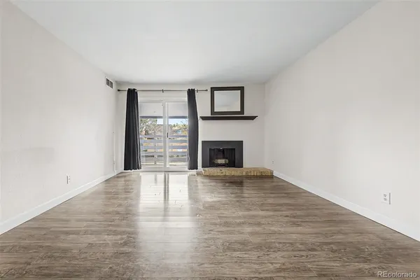 a view of an empty room with wooden floor fireplace and a window