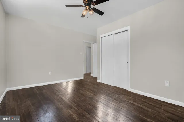 a view of an empty room with wooden floor and a ceiling fan