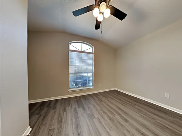 an empty room with wooden floor fan and windows