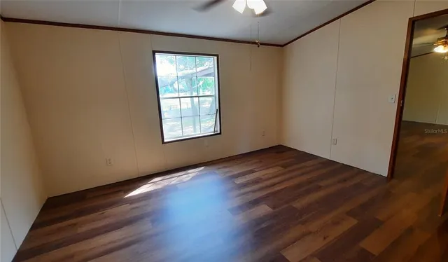 an empty room with wooden floor chandelier fan and windows