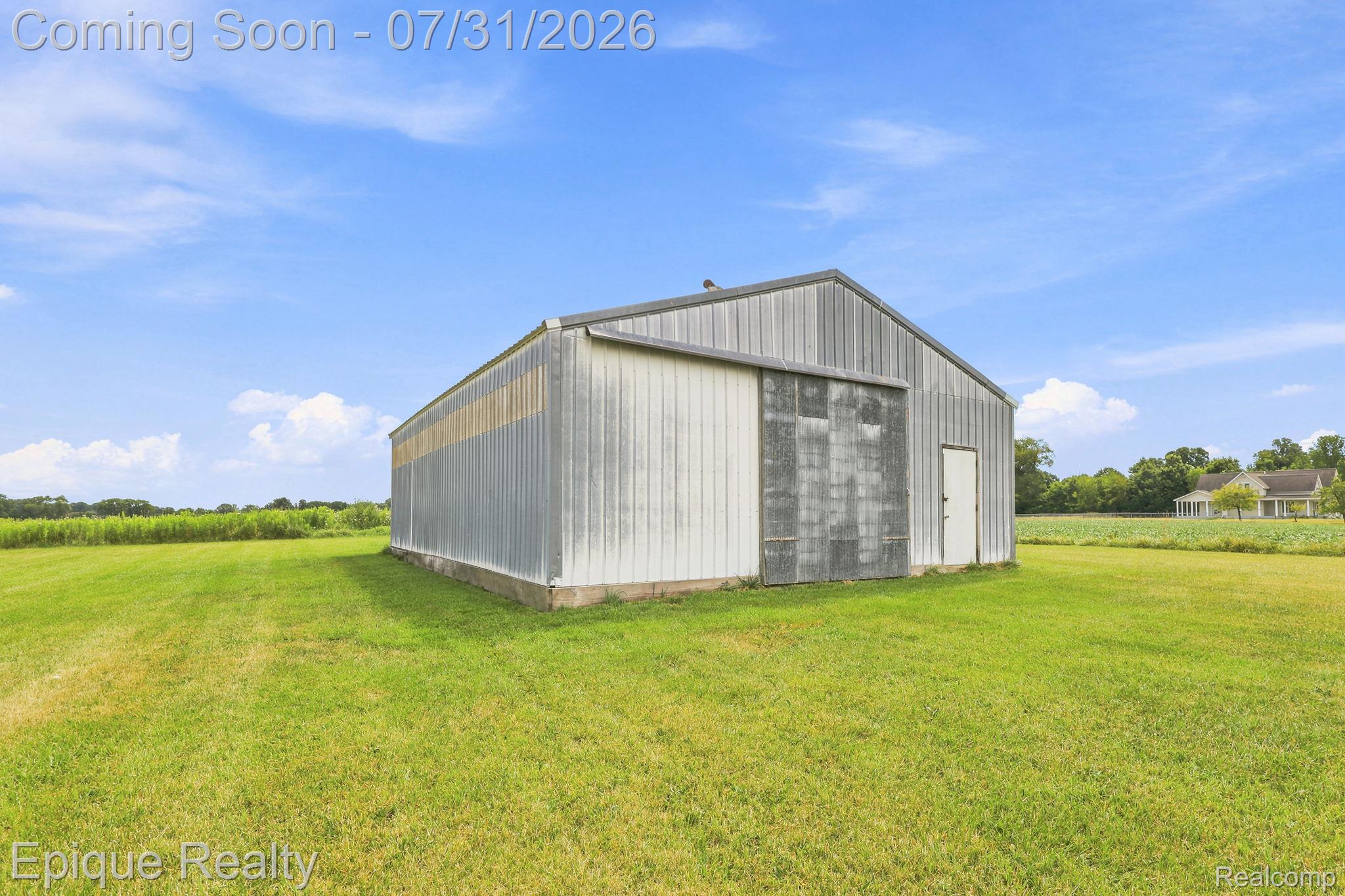 10179 Duffield Road Gaines, MI 48436 - Photo 24 of 30 Expansive outbuilding featuring a metal roof and siding, concrete foundation, large sliding door, and a standard entry door, set within a substantial grassy area