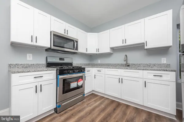a kitchen with stainless steel appliances granite countertop white cabinets a sink a stove and a microwave