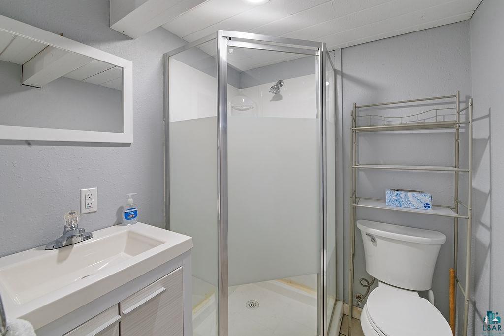 122 3rd Street Cloquet, MN 55720 - Photo 28 of 42 Compact bathroom featuring a glass-enclosed shower, white vanity with integrated sink, framed mirror, and a toilet