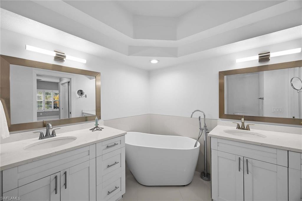 6834 Lantana Bridge Road, Unit 101 Naples, FL 34109 - Photo 31 of 50 a bathroom with a double vanity sink large mirror and bathtub