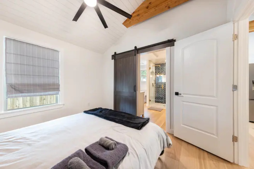2319 Santa Rita Street Austin, TX 78702 - Photo 9 of 26 Bedroom with light wood-style flooring, a barn door, ceiling fan, lofted ceiling with beams, and ensuite bathroom