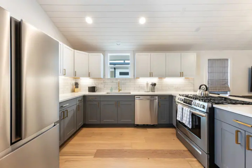 2319 Santa Rita Street Austin, TX 78702 - Photo 6 of 26 Two tone kitchen featuring two tone cabinets, stainless steel appliances, light wood-style flooring, tasteful backsplash, and a peninsula