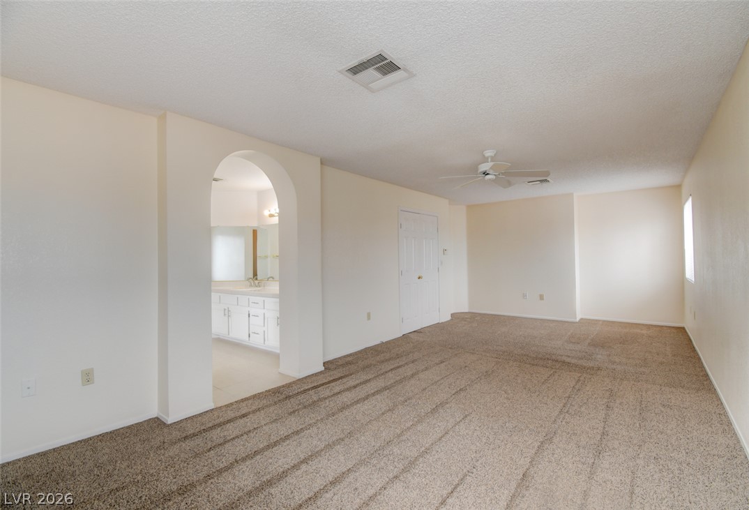 5 Tarryall Terrace Henderson, NV 89074 - Photo 34 of 44 A spacious primary bedroom featuring plush carpeting, an arched doorway leading to a well-appointed primary bathroom, and a ceiling fan for comfort.