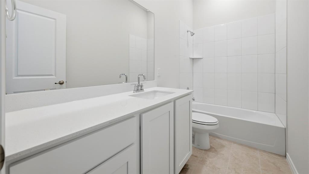 4163 Waldron Trail Forney, TX 75126 - Photo 16 of 30 Bathroom featuring a white vanity with an integrated sink and chrome faucet, a large wall-mounted mirror, a white bathtub with subway tile surround, and neutral-toned floor tiling