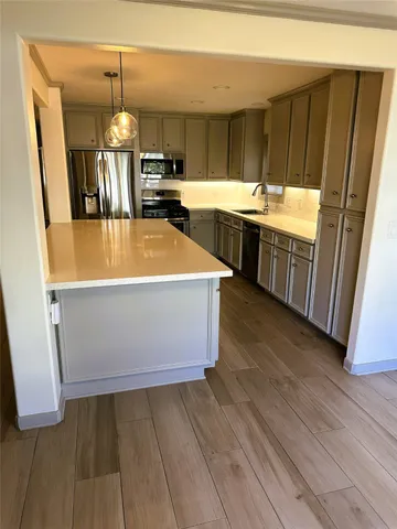 a view of a kitchen with kitchen island wooden floor stainless steel appliances and cabinets