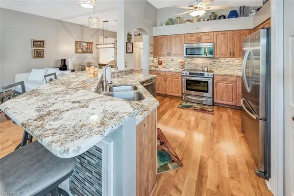 a living room with stainless steel appliances granite countertop a kitchen island a stove a sink dishwasher and a refrigerator with wooden floor