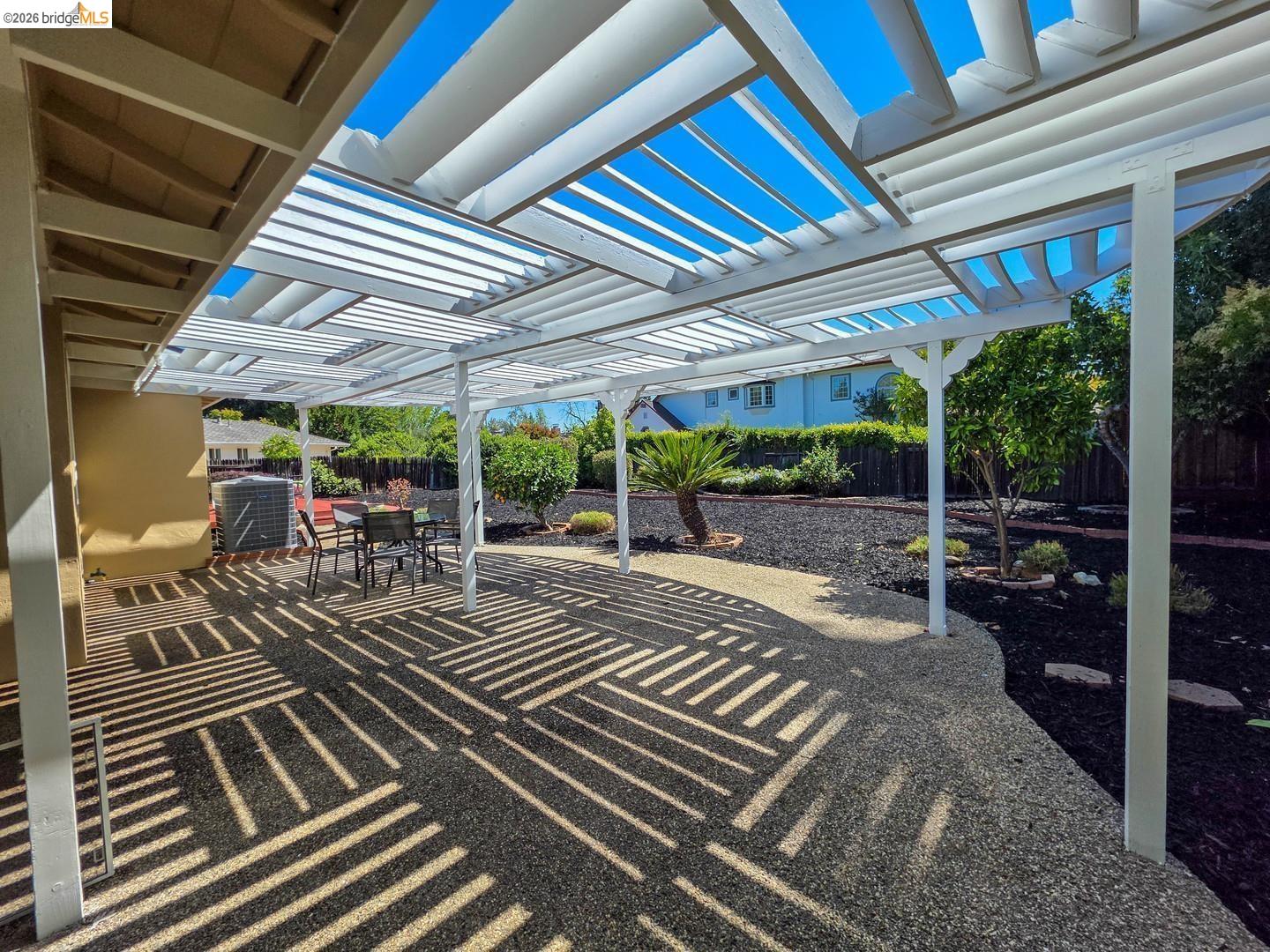 965 Springer Road Los Altos, CA 94024 - Photo 20 of 31 Expansive outdoor patio featuring a white slatted pergola, pebble aggregate surfacing, and surrounding landscaped garden beds