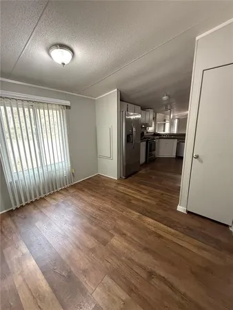 an empty room with wooden floor and a kitchen