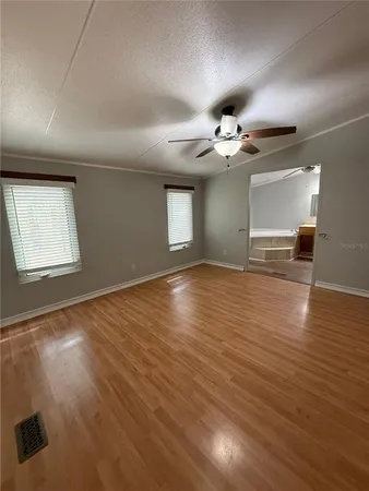 an empty room with wooden floor chandelier fan and windows