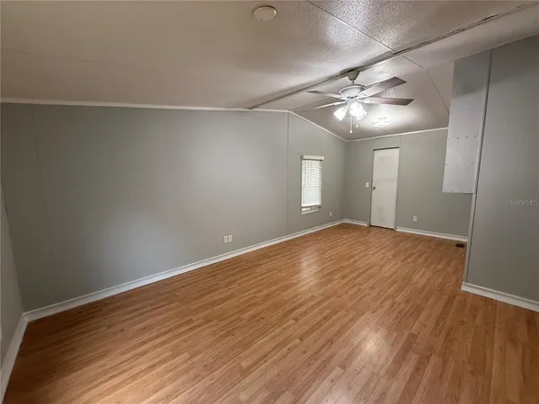 an empty room with wooden floor chandelier fan and windows