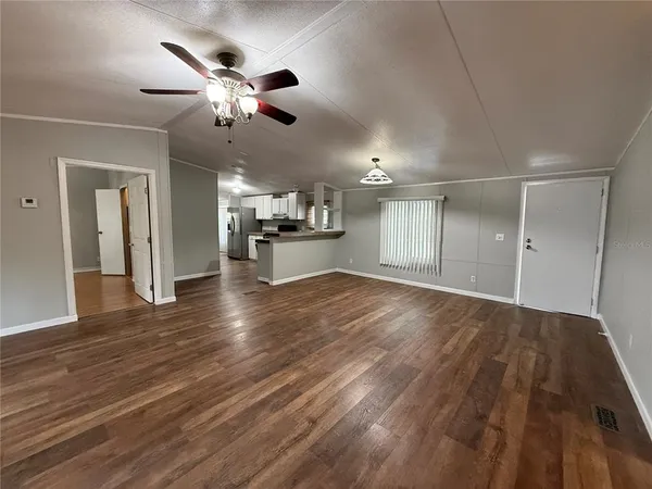 a view of an empty room and kitchen view with wooden floor