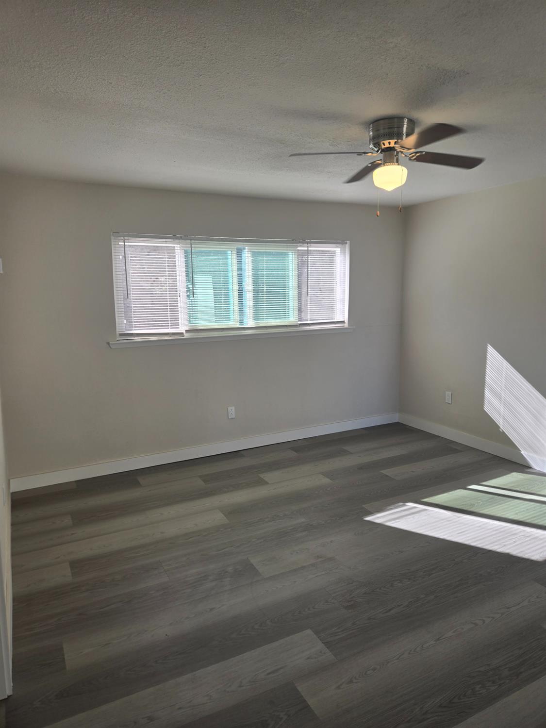 a view of an empty room with wooden floor and a window