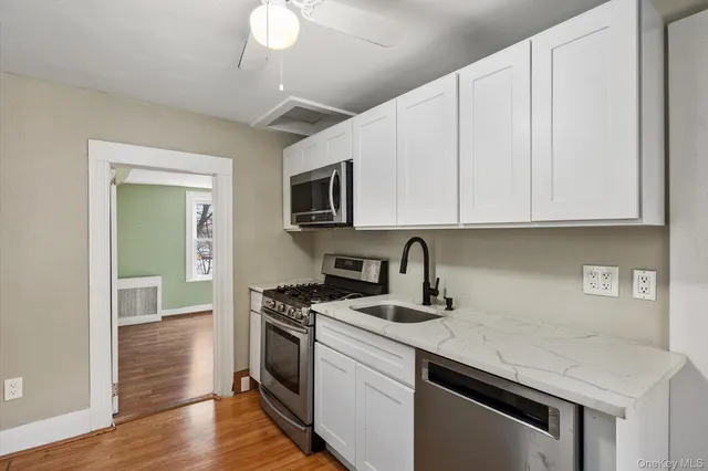 a kitchen with granite countertop a stove top oven a sink dishwasher and white cabinets with wooden floor