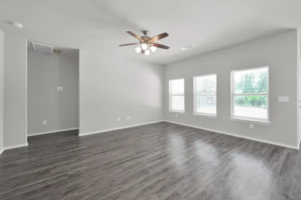 an empty room with wooden floor fan and windows