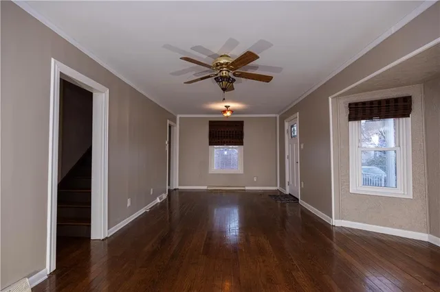 a view of a livingroom with wooden floor a ceiling fan and windows
